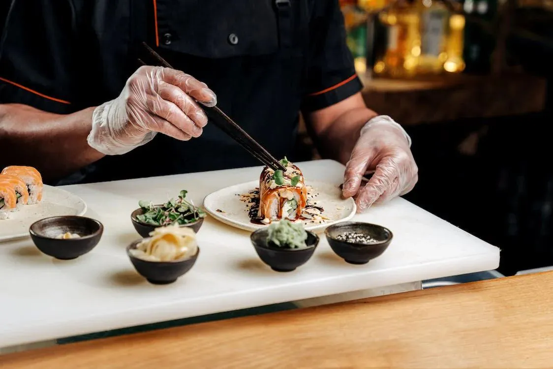 Chef carefully garnishing a salmon sushi roll with microgreens at YUKI Sushi & Wok, an Asian Fusion Restaurant in Wayne